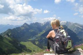 Nuori nainen istuu selin reppu selässä, katse kohti vuorimaisemaa
