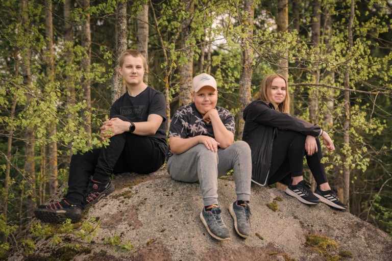 Kolme nuorta istuu mietteliäinä kivellä metsässä.