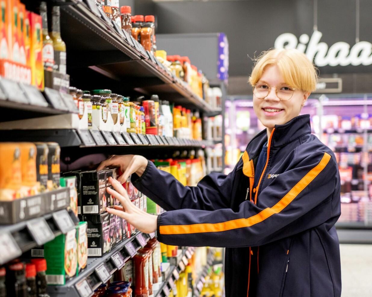 Aatu asettelee säilykepurkkeja kaupassa hyllyjen välissä.